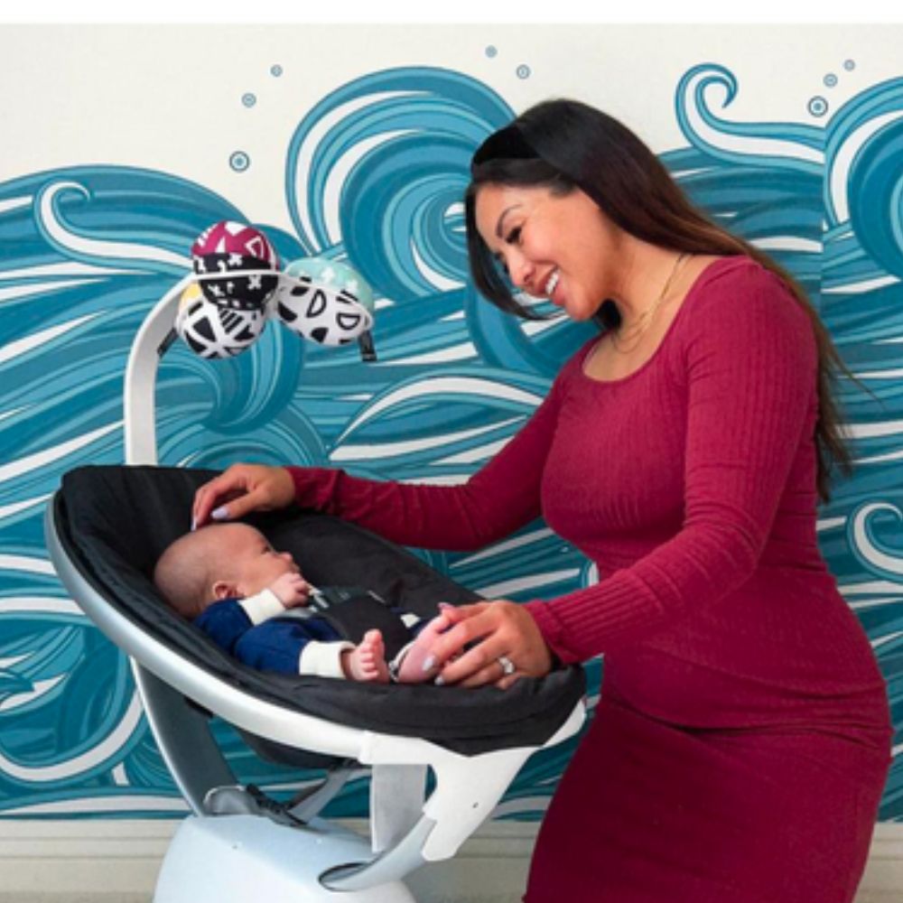 Woman with a baby in a black baby seat against a blue wave-patterned wall.