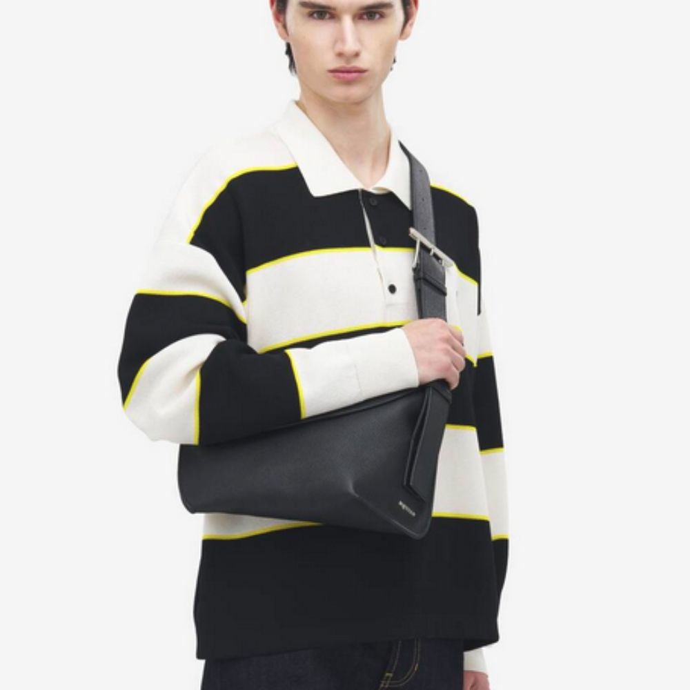 Person wearing a black, white, and yellow striped sweater holding a Alexander McQueen Large T-Bar Sling Bag in Black Leather on a white background