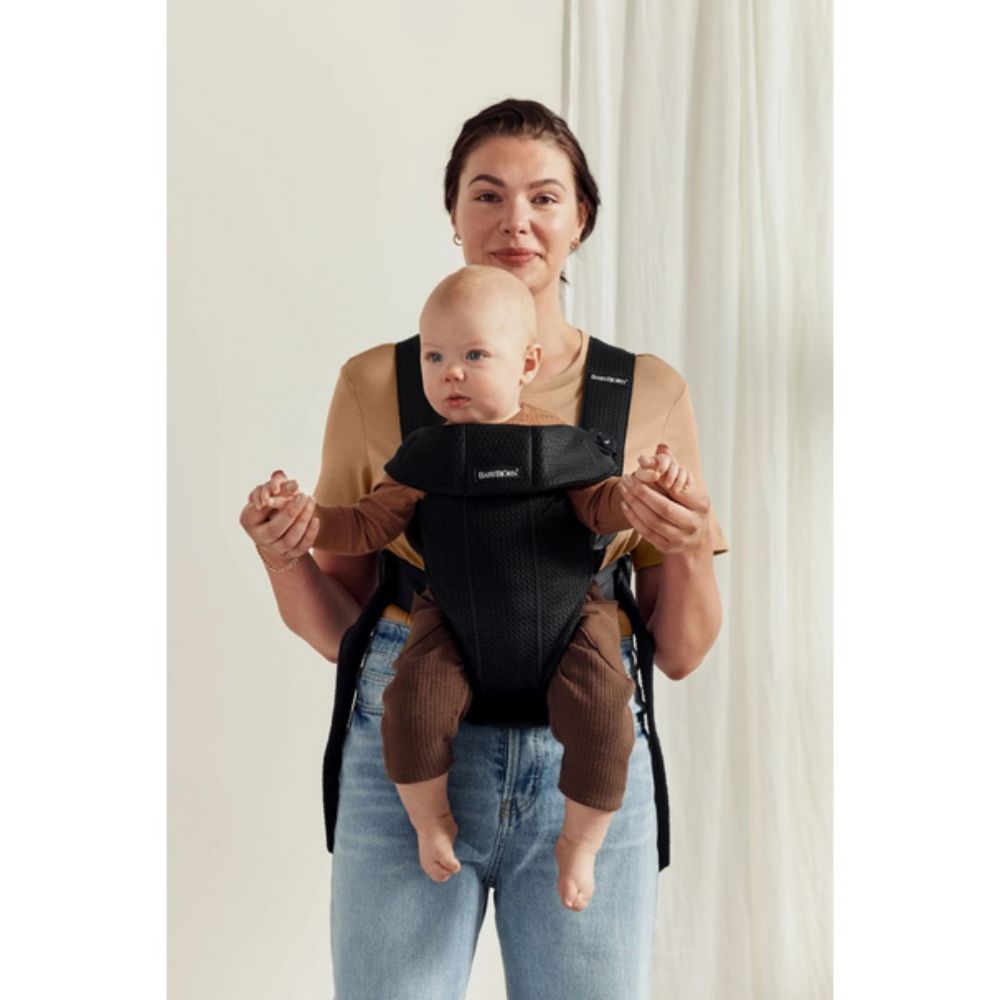 Woman holding a baby in a black and brown baby carrier against a white background