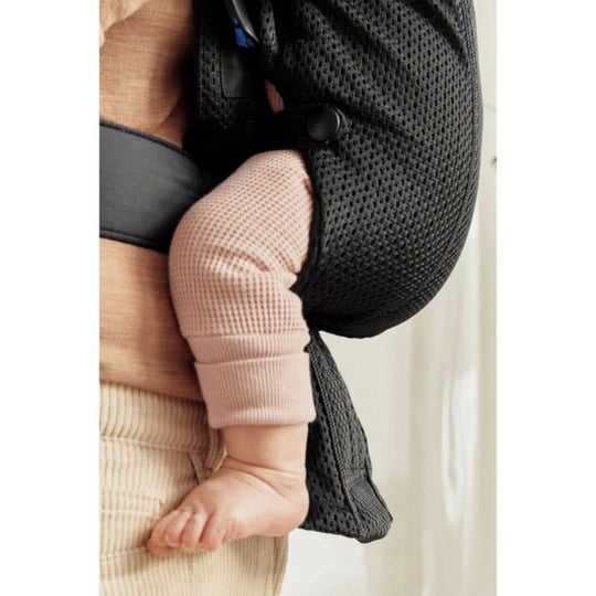 Baby in a black carrier with pink pants and beige blanket