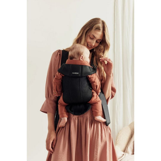 Woman wearing a baby in a black baby carrier against a white background