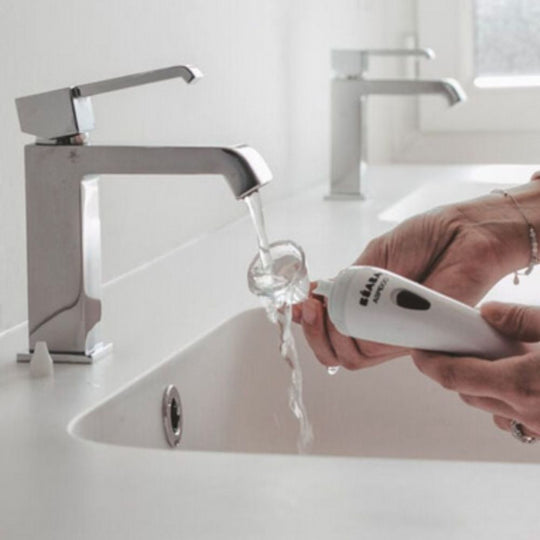 Person washing Beaba Aspidoo Nasal Aspirator under water flow from a faucet in a bathroom setting.