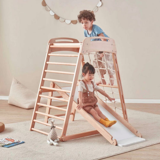 Children playing on a wooden climbing toy with a slide in a room.