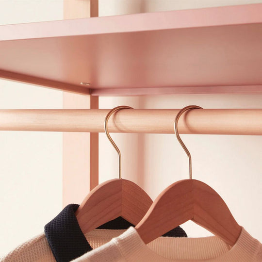 Wooden hangers with clothes on a pink shelf