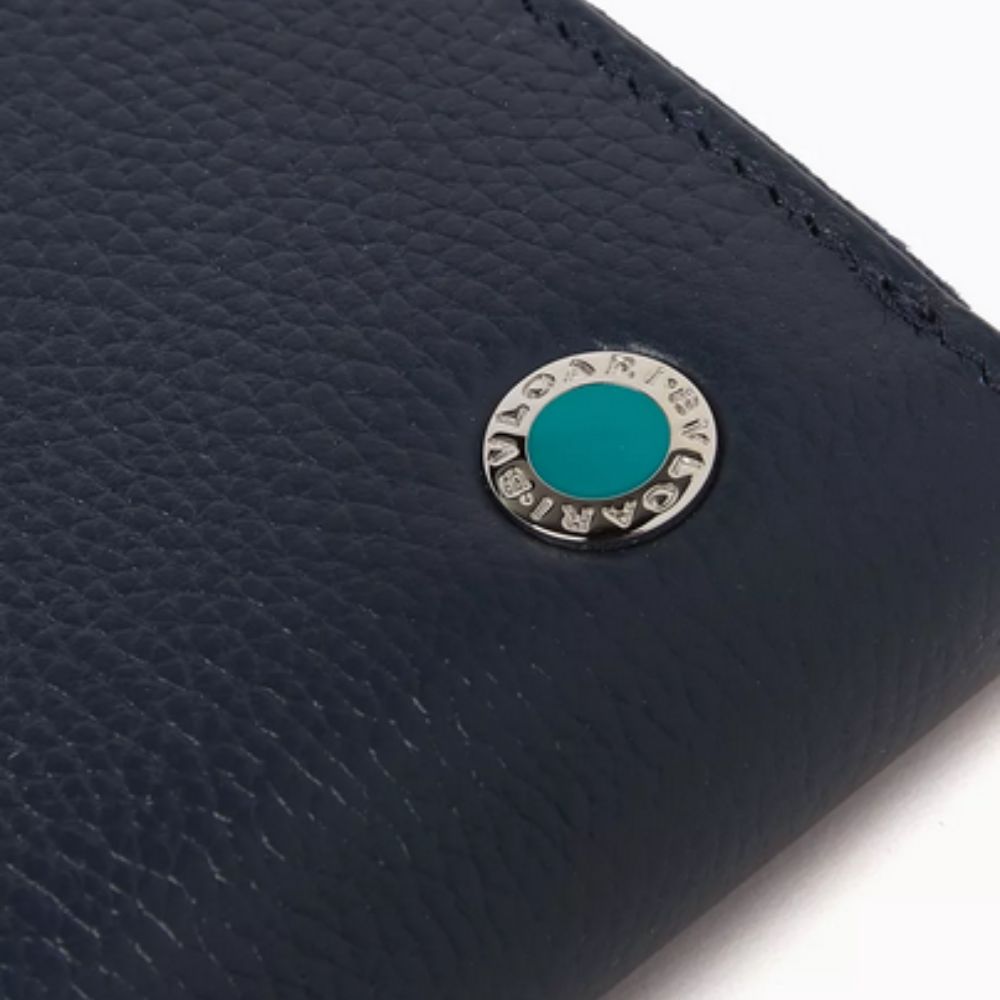 A close-up shot of a dark blue, textured leather wallet, featuring a prominent circular silver-toned BVLGARI logo hardware with a bright teal center.