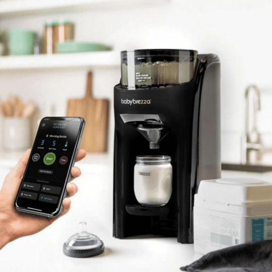 Babybrezza formula dispenser with smartphone app control on a kitchen counter.