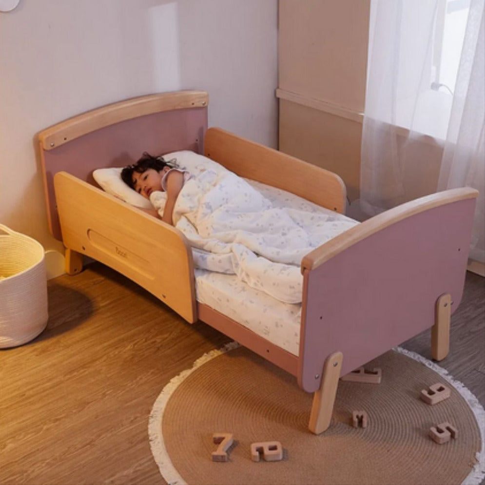 Child sleeping in Boori Neat 5-in-1 Convertible Cot in a room with toys on the floor.