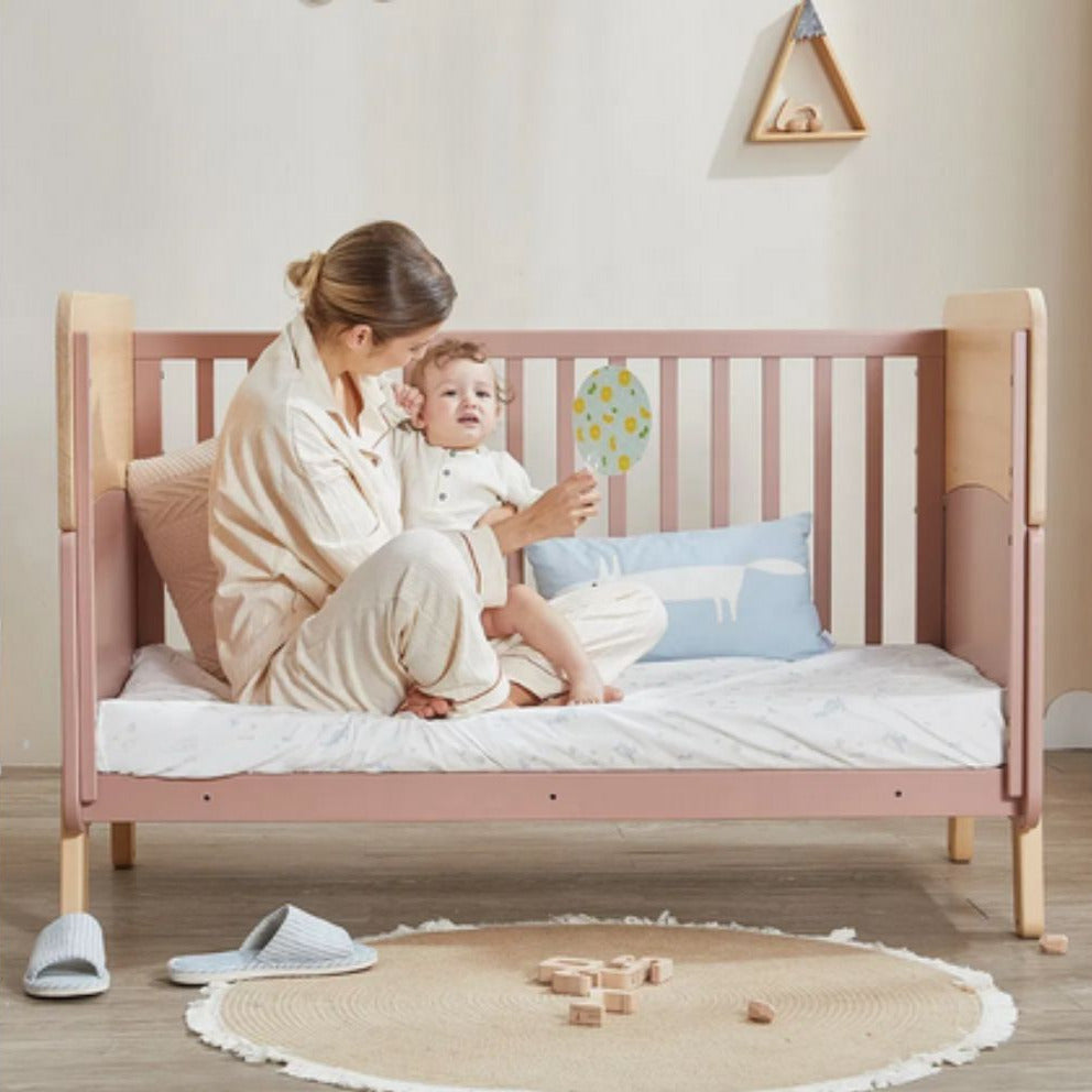 Woman and child in Boori Neat 5-in-1 Convertible Cot with wooden toys on the floor.
