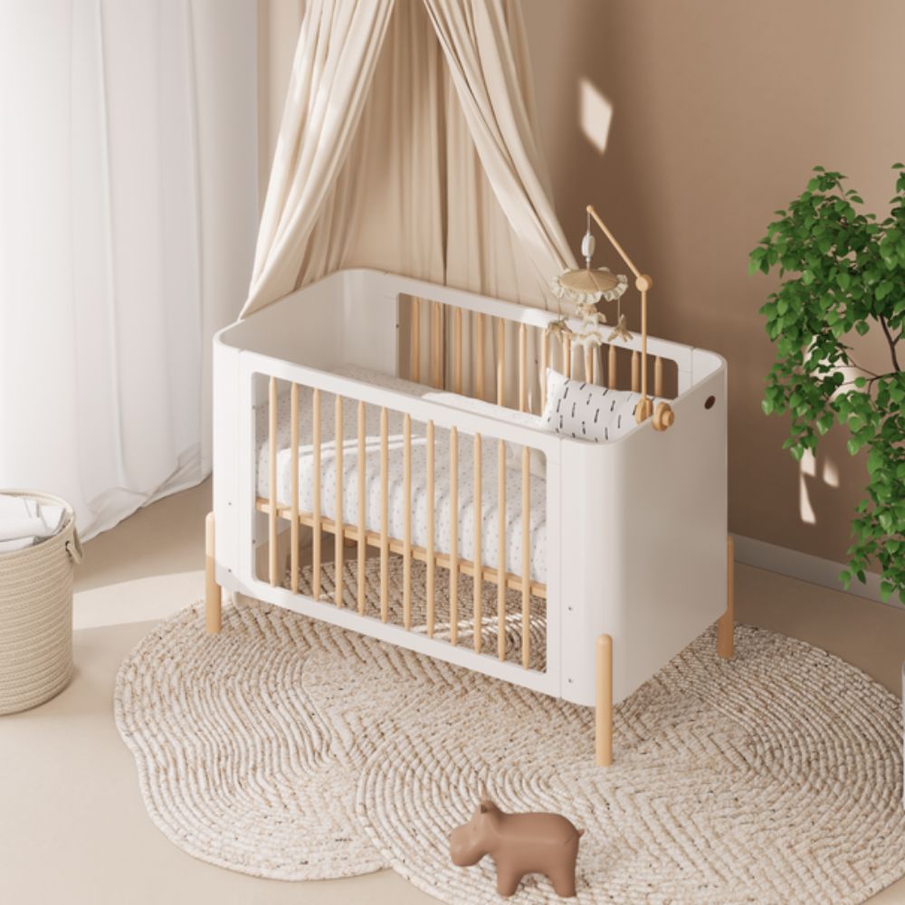 Boori Nova Cot Bed - Modern Two-Tone Toddler Convertible in Barley White & Beech in a nursery setting with a plant and rug.