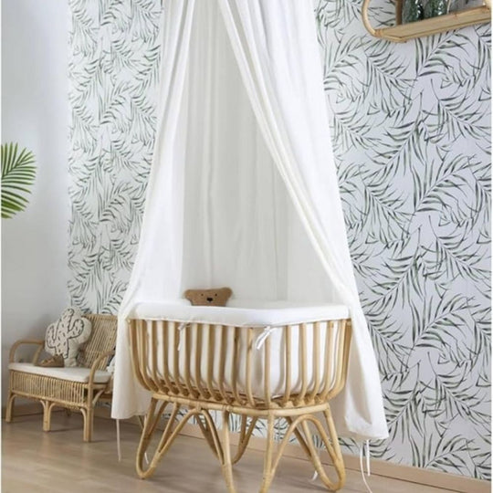 Wooden crib with canopy in a room with leaf-patterned wallpaper