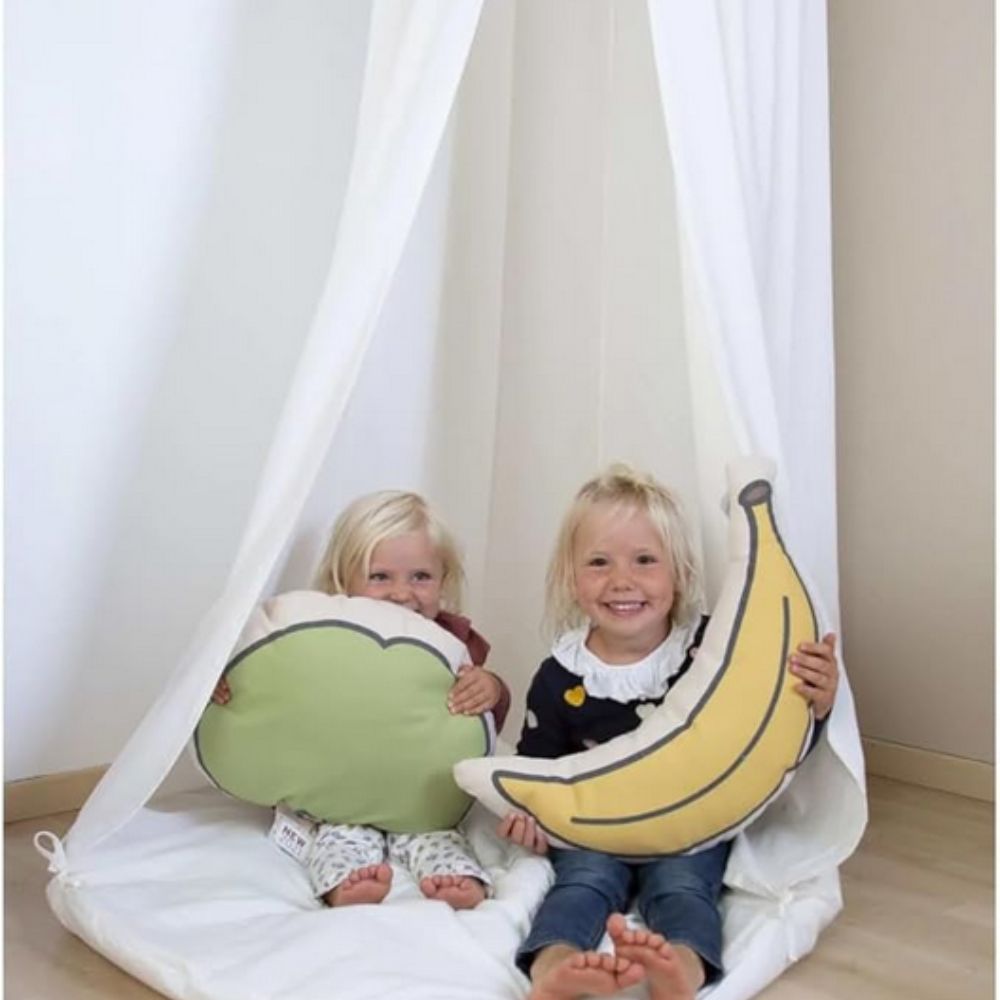 Two children sitting inside a white play tent holding pillow props shaped like broccoli and a banana.