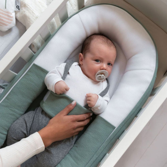 Baby in a green and white baby seat with a pacifier, held by an adult.