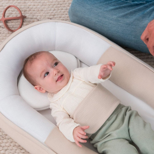 Baby lying in a white Cocoon with a person partially visible in the background