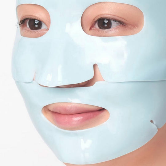 Close-up of a person wearing a light blue, two-piece rubber sheet mask that covers the forehead, eyes, nose, cheeks, and chin. Their dark brown eyes are visible through the eyeholes, and their lips are slightly parted, revealing a hint of pink. The mask has a smooth, slightly reflective surface.