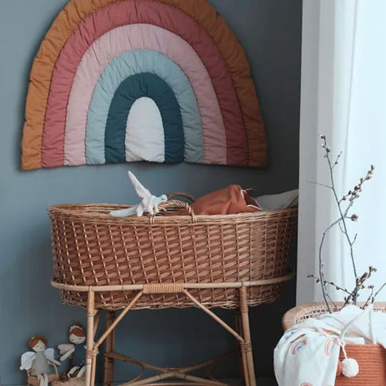 Decorative Fabelab Blanket with Rainbow on wall hanging above a wicker crib in a nursery