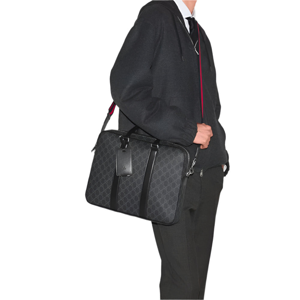 A person wearing a dark gray hooded sweatshirt with a white shirt and dark tie underneath, and dark trousers, stands holding a black Gucci GG Supreme Canvas Medium Briefcase. The person's face is not visible. The briefcase, held by its top handle and also worn with a shoulder strap, features the dark gray GG monogram pattern. A black leather luggage tag hangs from one of the handles.