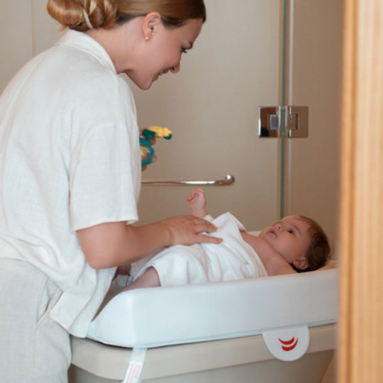 Woman bathing a baby in a sink with a towel draped over the edge.