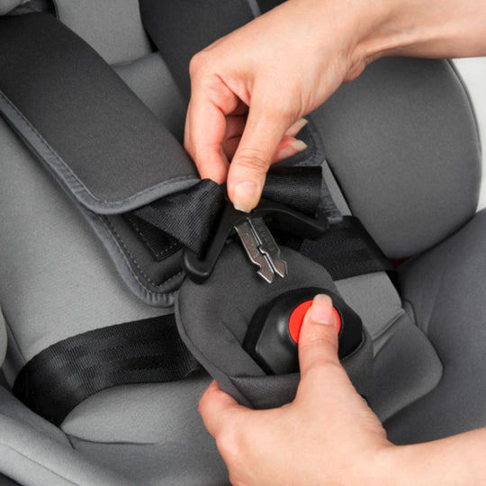 Person adjusting a car seat belt buckle on a gray car seat.