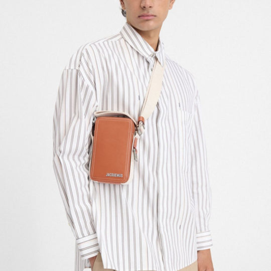 A light brown Jacquemus Vertical Cuerda cross-body bag with a cream strap, worn by a person in a white and grey striped long-sleeved shirt.