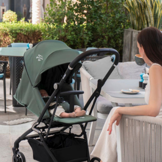 Woman sitting at an outdoor cafe with a Jikel Life 360 Reversible Stroller next to her