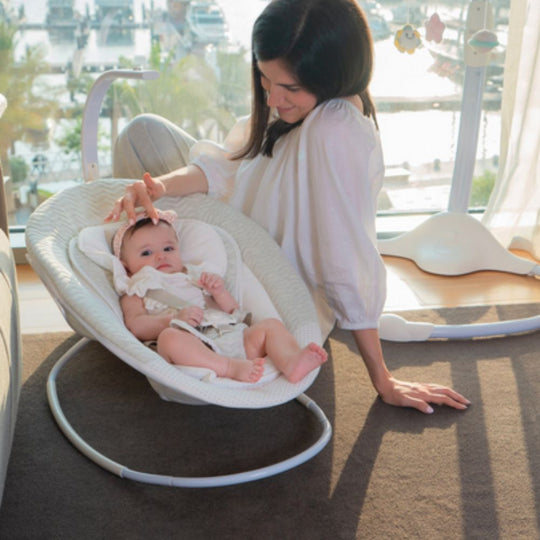 Woman with a baby in a white baby bouncer in a bright room.