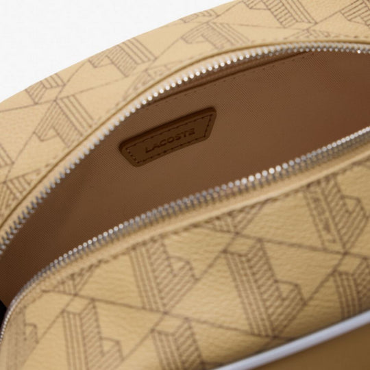 An overhead, slightly angled close-up of the open Lacoste The Blend Grained Texture Vanity Bag, showing its beige monogram-printed canvas exterior and a light beige interior with a leather patch embossed with "LACOSTE".