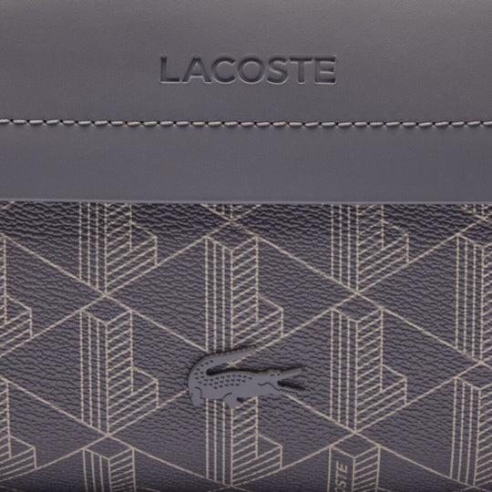Close-up shot focusing on the details of the LACOSTE The Blend Toiletry Bag. The image prominently displays the signature Lacoste crocodile logo in a dark, tonal shade, positioned over the bag's patterned canvas.