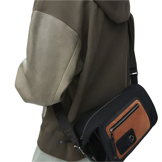 A person from the chest down wears a dark olive green hoodie with light green patches on the shoulders and arms. They are carrying a black LOEWE Small Flex Loop Bucket bag diagonally across their body.