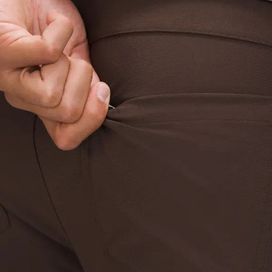 A close-up of a man's brown Lululemon ABC Warpstreme Slim-Fit 5 Pocket Pants with a hand in the back pocket. The pants have a secure zip pocket.