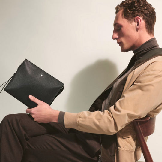 Man holding a black leather clutch bag against a plain background
