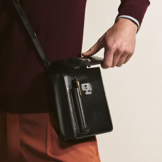 Person holding Montblanc Meisterstück Small Messenger Bag with Integrated Pen Case with a pen inside, wearing a burgundy coat.