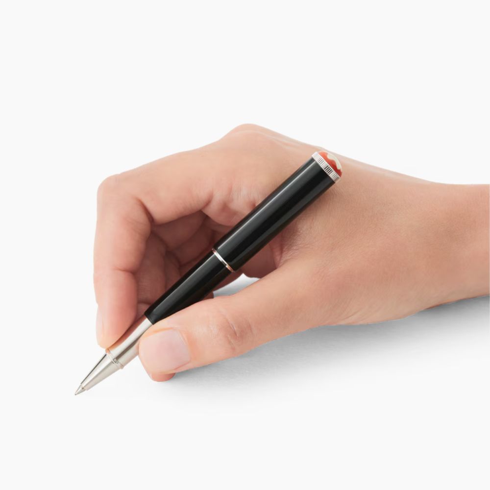 Close-up of a hand writing with a Montblanc Heritage Rouge et Noir "Baby" Special Edition pen, showing the black lacquer barrel, silver trim, and red and white cap detail.