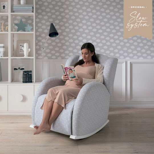 Woman reading a book in a Micuna - White & Galaxy Grey Flor Slow System Reclining Nursing Chair in a cozy room.