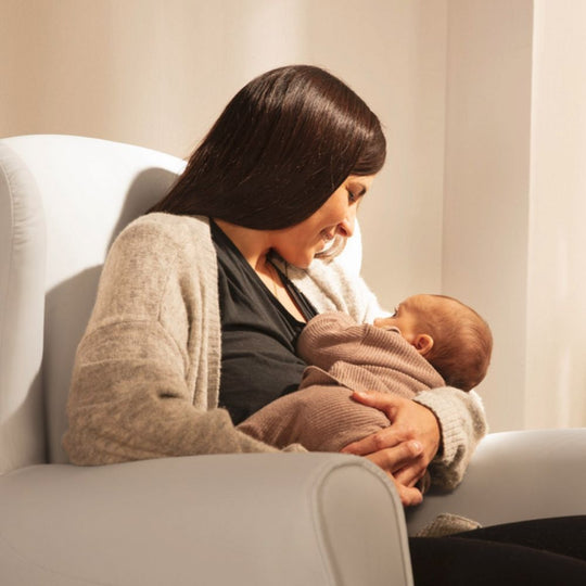 Woman holding a baby in a cozy indoor setting reclining on a Micuna Flor Slow System Rocking Chair