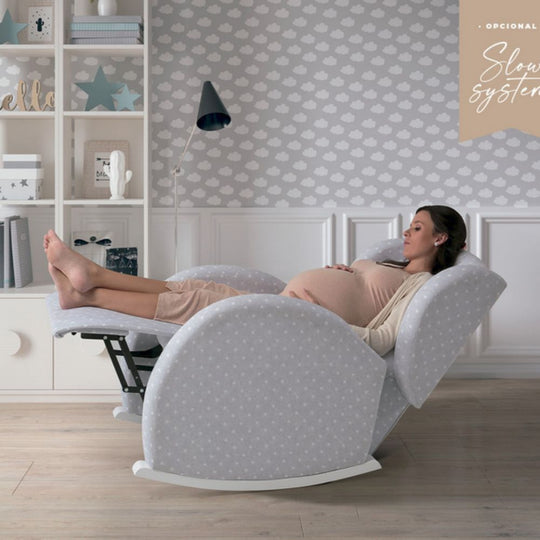 Pregnant woman relaxing in a Micuna Flor Slow System Rocking Chair with cloud-patterned wallpaper in the background