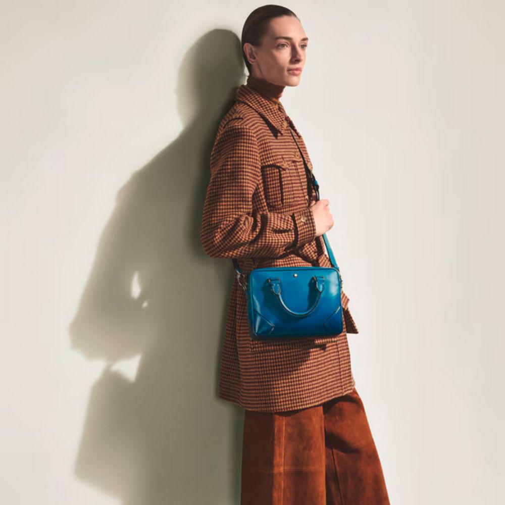 Person wearing a brown coat and holding a Montblanc Meisterstück Sfumato Blue Leather Mini Document Case against a white wall