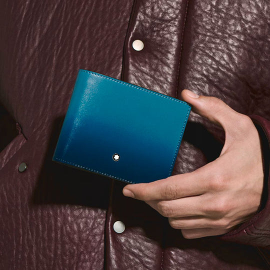 Hand holding a Montblanc Meisterstück Sfumato Smoky Blue Leather 6-Card Wallet against a brown leather background
