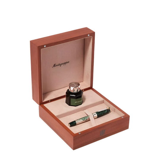 A Montegrappa fountain pen with a green marbled barrel and silver cap, a green ink bottle with a silver cap, both nestled in a light wood presentation box with a beige suede-like interior and the "Montegrappa" logo printed inside the lid.