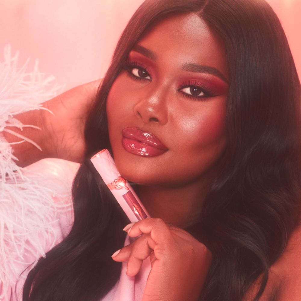 A model holds a Charlotte Tilbury lip gloss tube. She has a matching pink eye shadow.