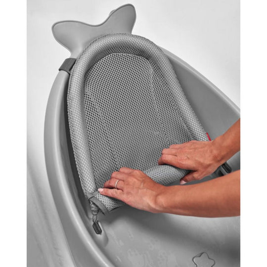 Gray baby bath seat with shark fin design, showing a person adjusting the mesh cushion.