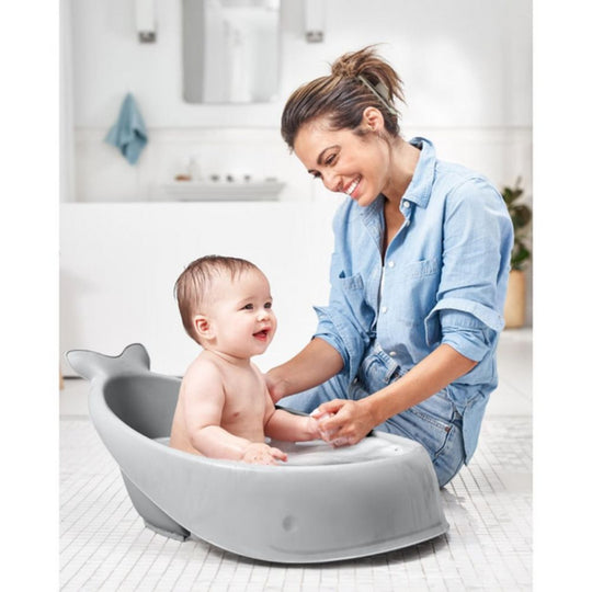 Woman bathing a baby in a gray bathtub in a bathroom.