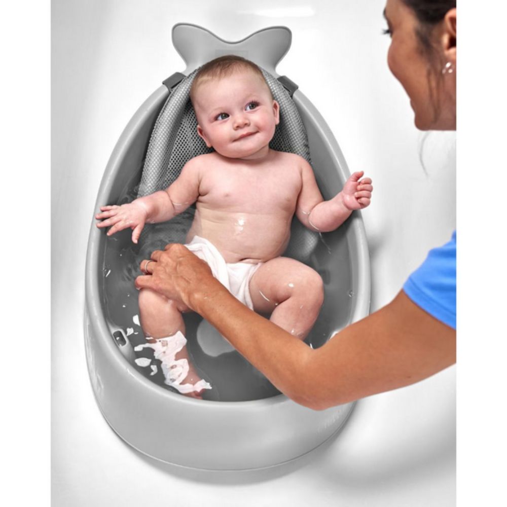 Baby sitting in a shark-shaped bathtub with a person assisting.