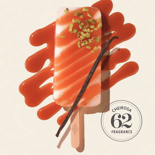 A stylized image featuring a popsicle with a swirled white and orange design, topped with chopped pistachios. A vanilla bean lies across the popsicle, and a swirl of caramel-colored liquid is around it. A circular stamp in the corner reads "Cheirosa 62 Fragrance".