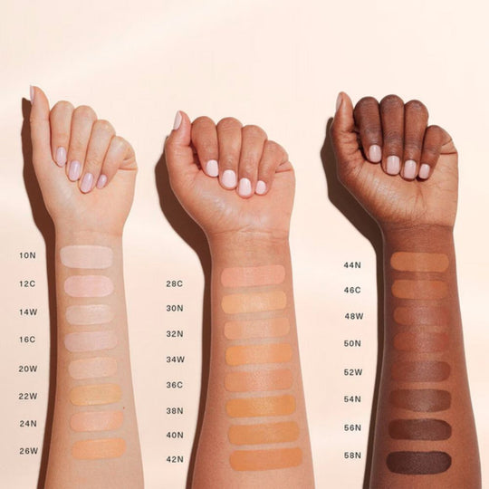 Three forearms, showcasing a range of skin tones, are positioned vertically against a light, neutral background. Each forearm has multiple swatches of liquid foundation or tinted moisturizer applied in vertical strips, demonstrating various shades.