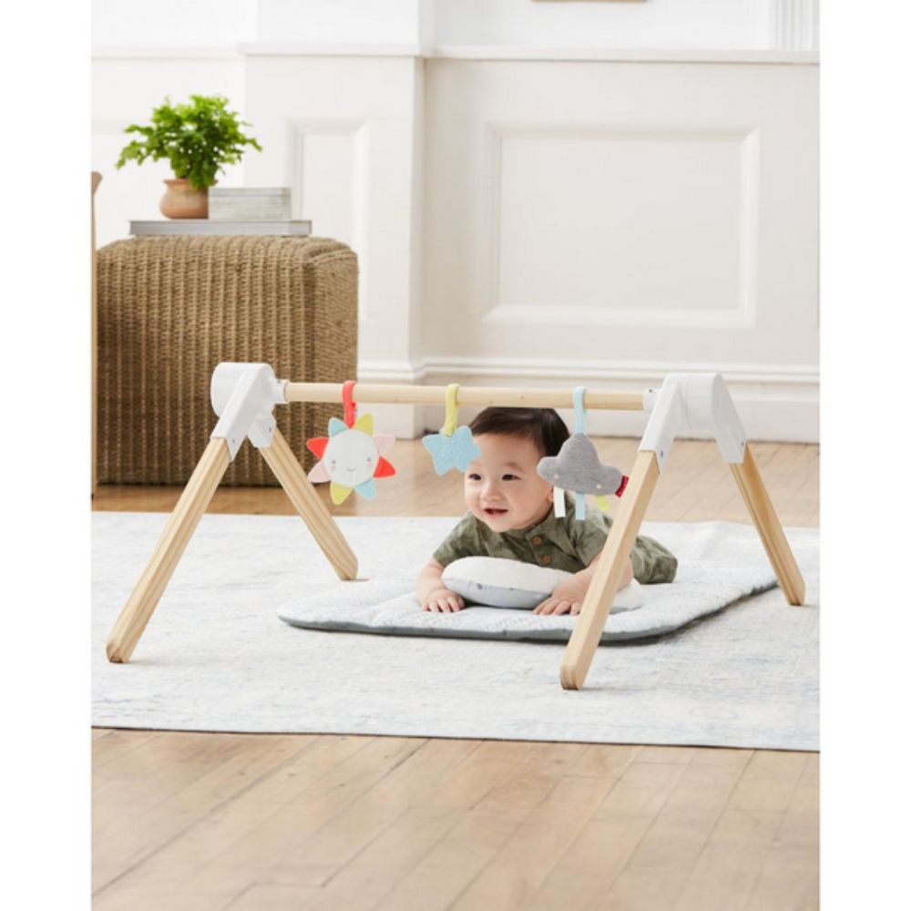Baby playing with Skip Hop Comfy Plush Wooden Activity Gym on a rug in a room.