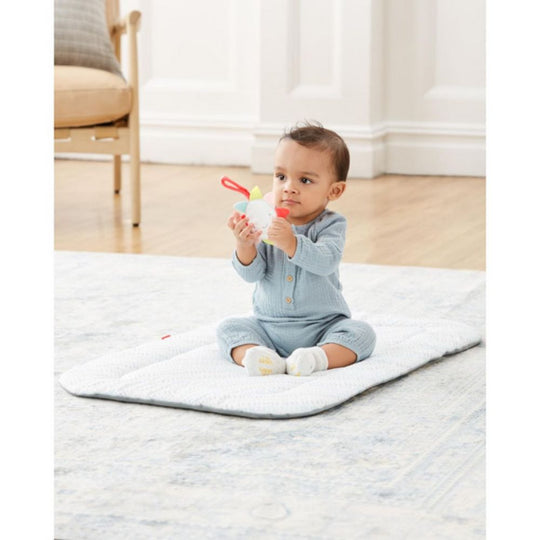 Baby sitting on a mat holding a toy in a room with a chair and white wall.