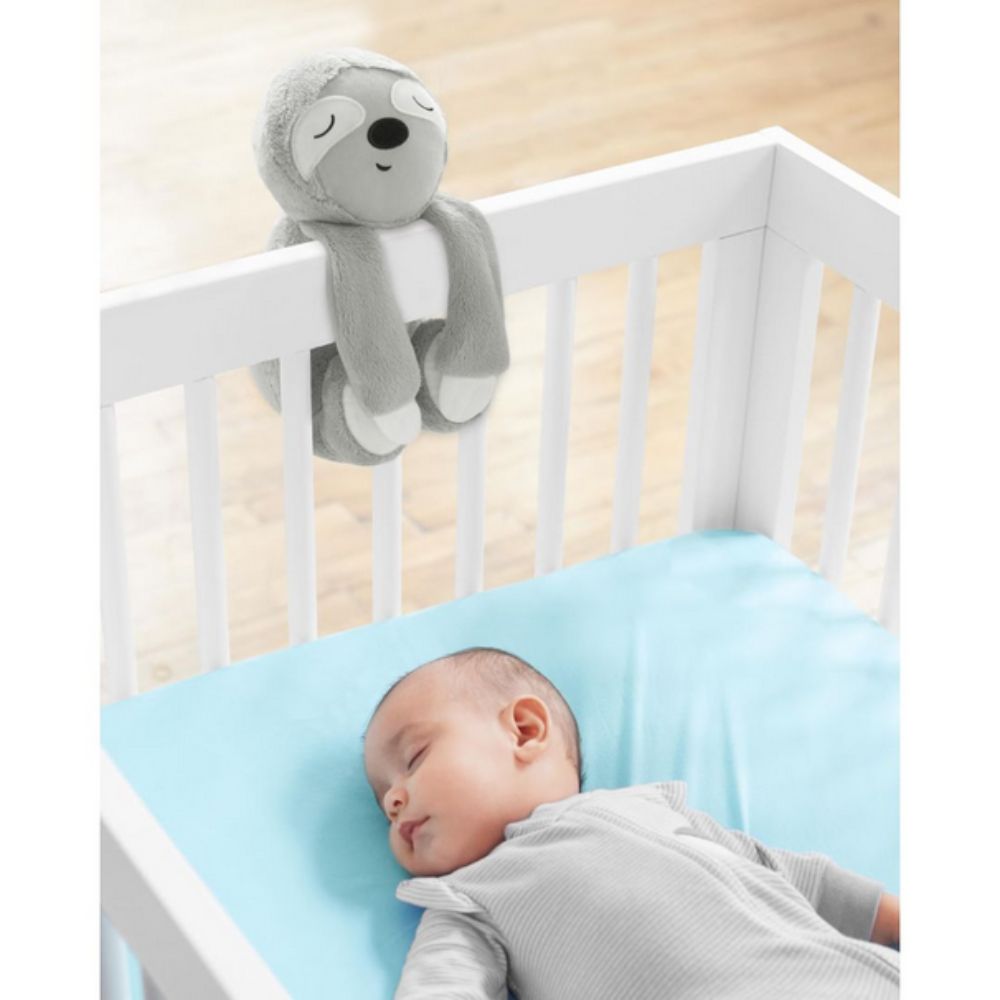 Baby sleeping in a crib with a gray plush toy above