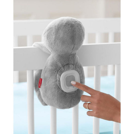 Gray plush toy with a button being pressed by a hand in front of a crib.