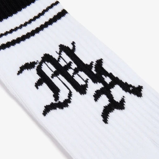 Close-up of the black and white "MA" logo on a white AMIRI sock with black stripes at the top