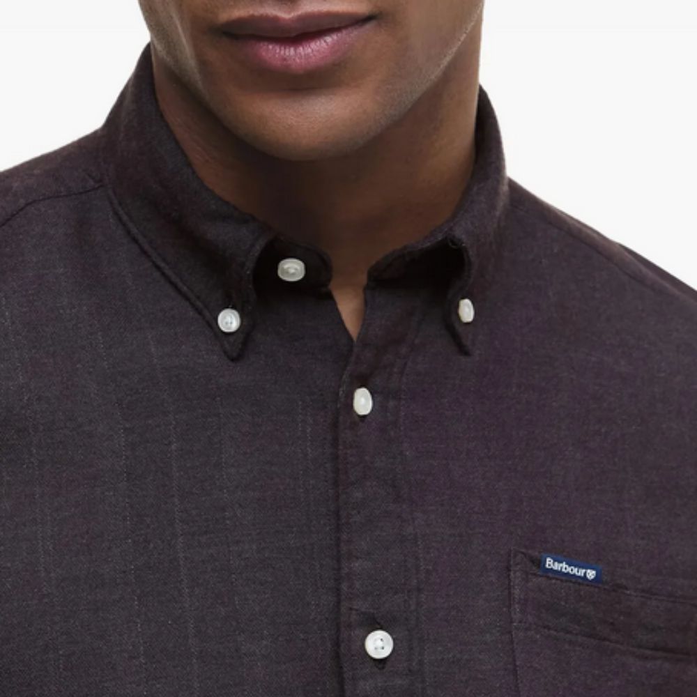 Close-up of a person wearing a dark brown button-up shirt with a visible brand logo.